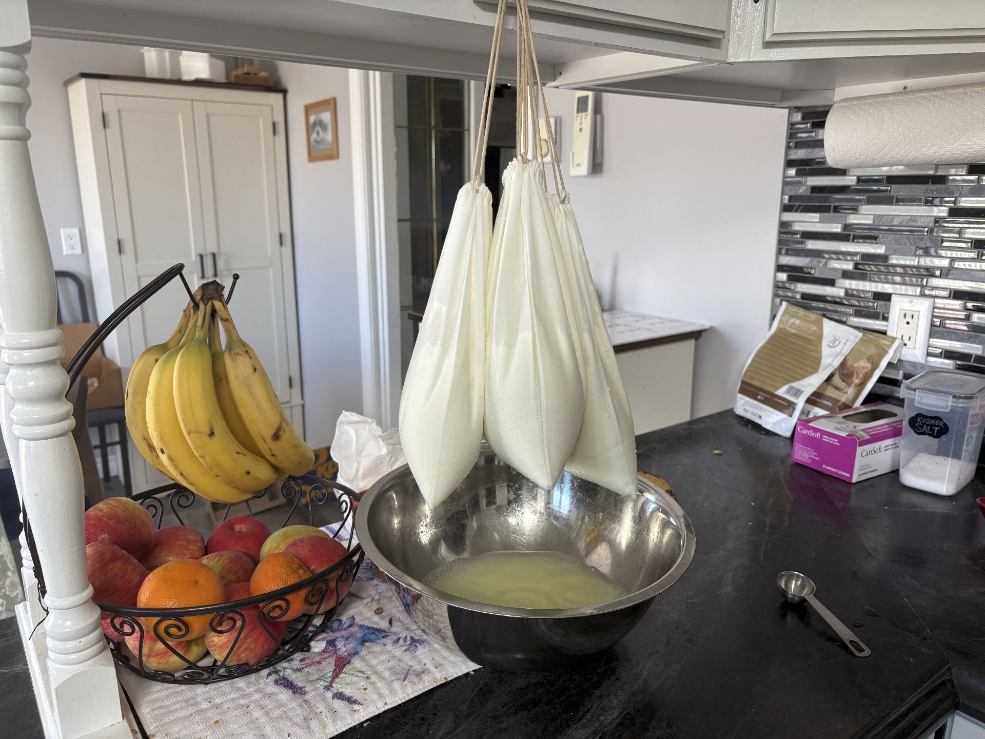 Paneer draining in cloth bags over a bowl.