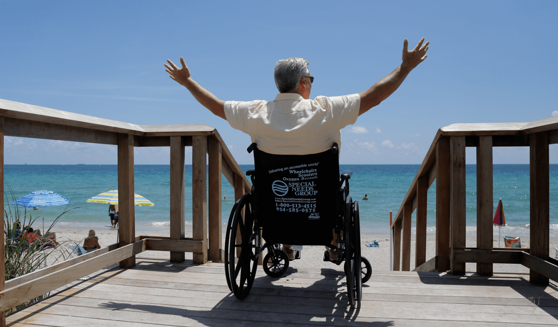 Man on pier sitting in wheelchair facing the beach and ocean