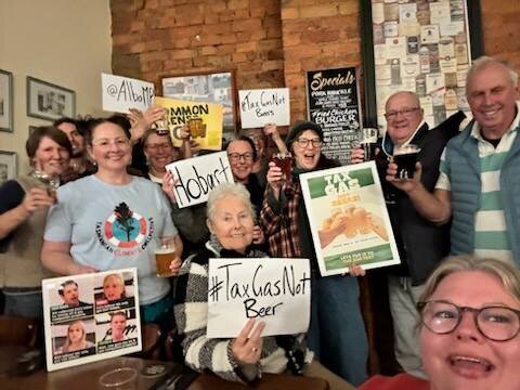 TCC folk and friends in a pub smiling and holding signs of #taxgasnotbeer
