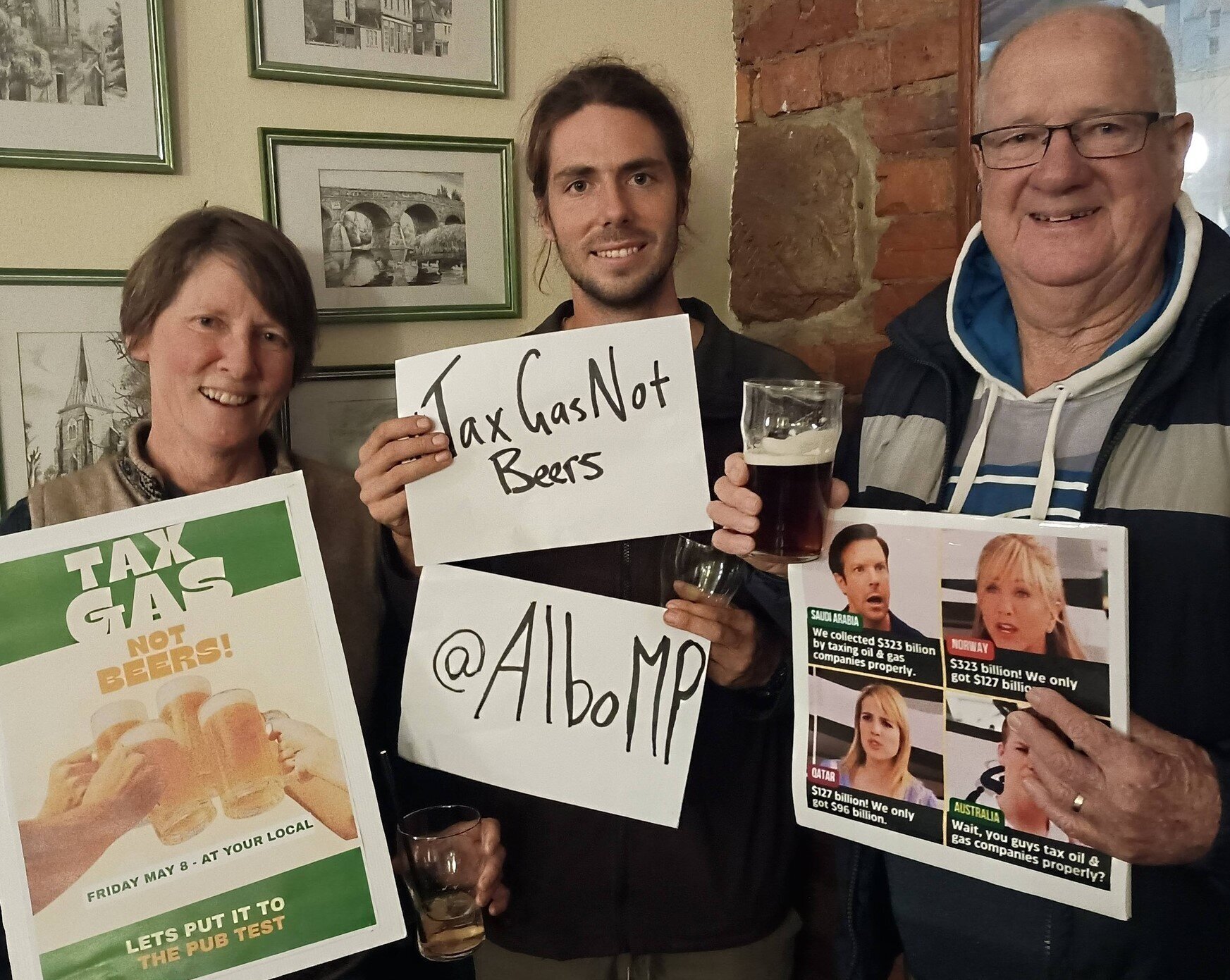 TCC folk and friends in a pub smiling and holding signs of #taxgasnotbeer