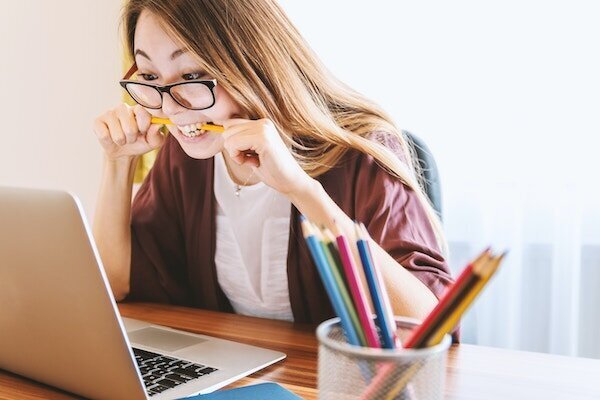 A photo of a woman leaning over a laptop biting a pencil in frustration or anxiety