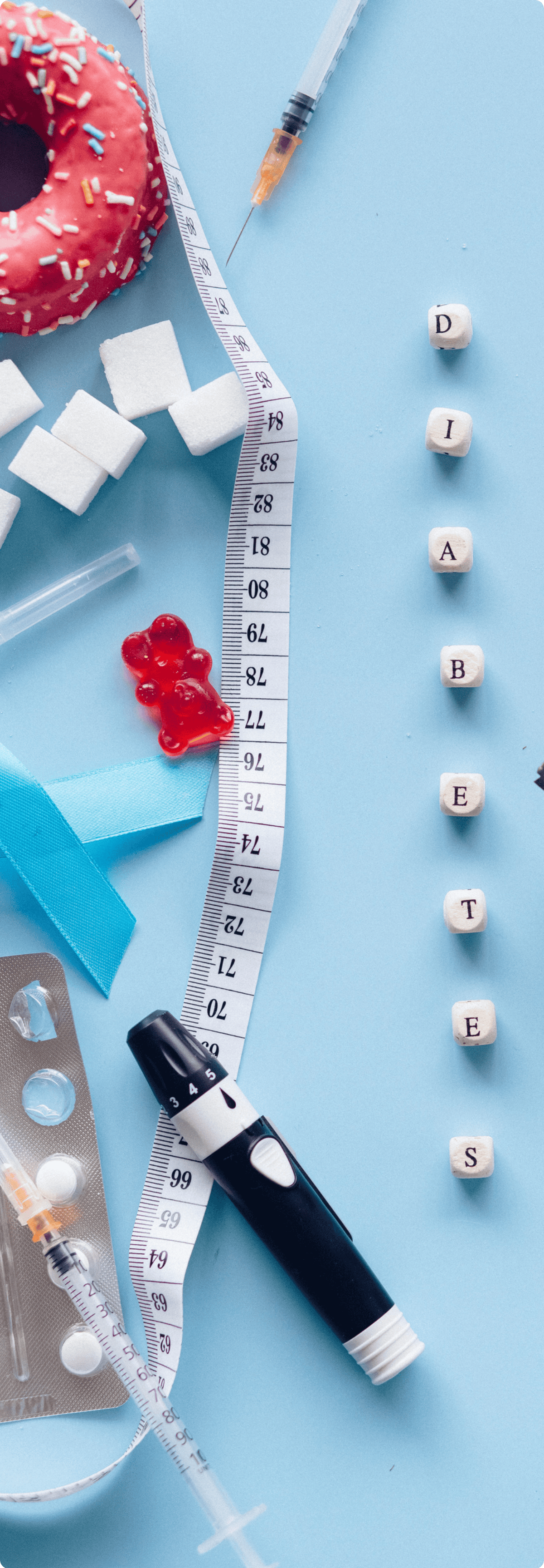 A flat lay of items related to diabetes management including a blood glucose meter, syringes, sugar cubes, a donut, and fruits, with wooden cubes spelling out "DIABETES".